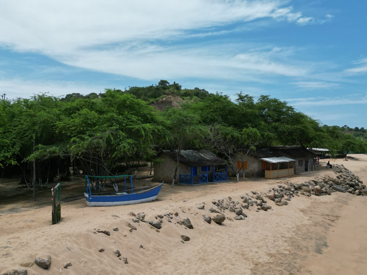 Barco azul ancorado na areia junto a casas de praia sombreada por árvores